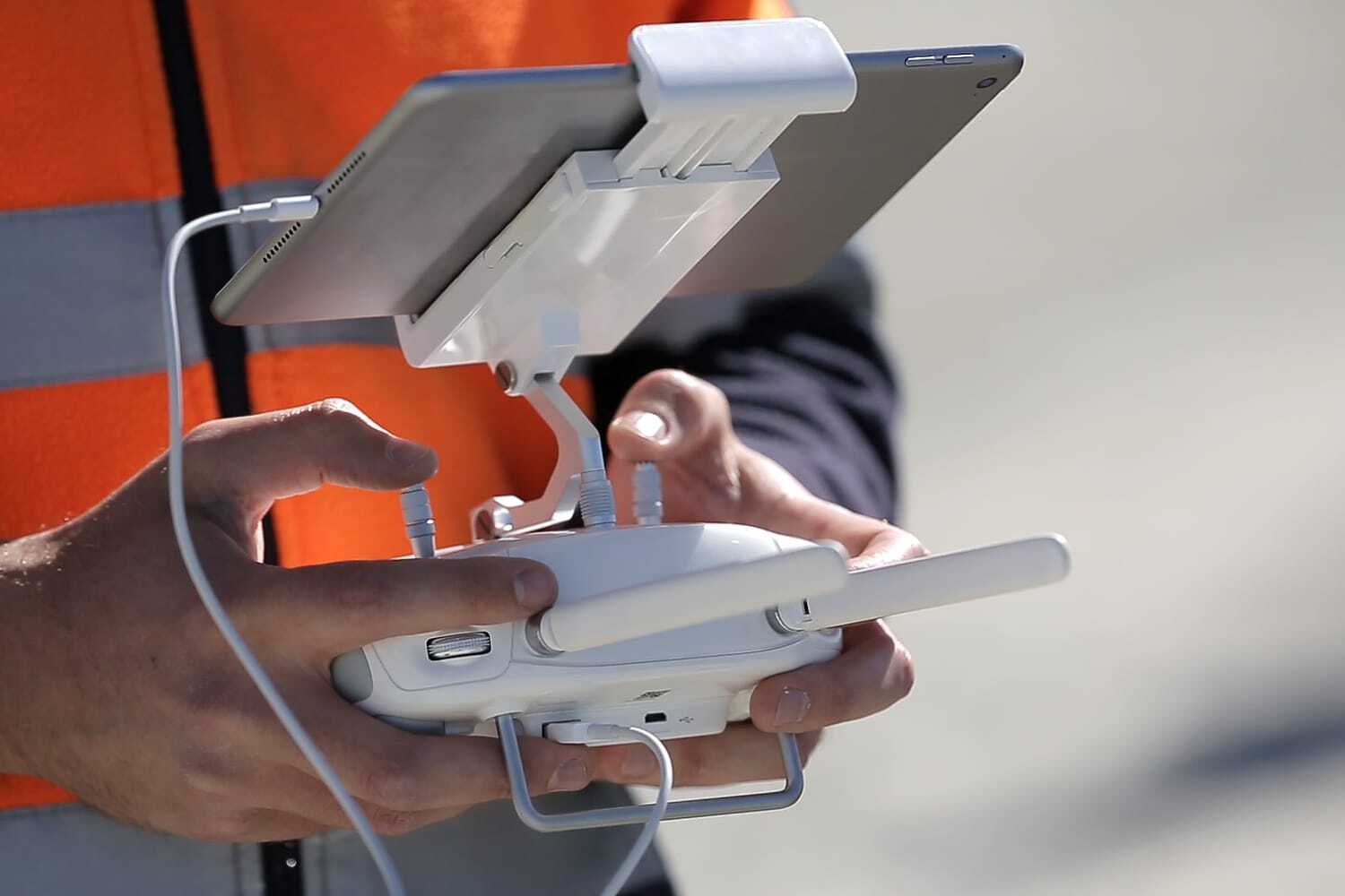 A man in a hi-vis vest holding a drone controller and viewing on a tablet.