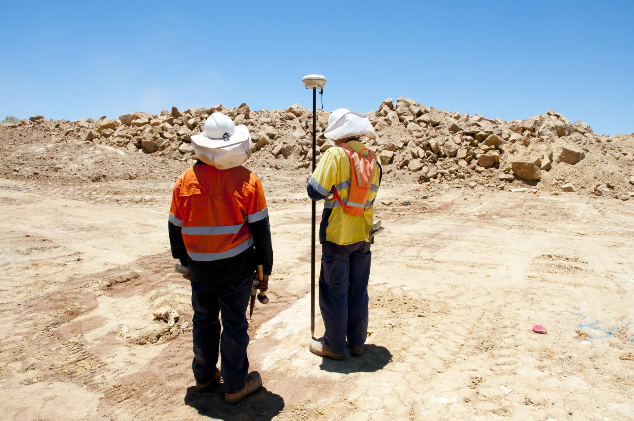 Two surveyors on a dirt track holding surveying equipment.