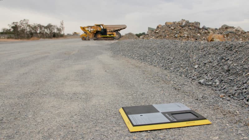 An AeroPoint sat on the ground on a track with an earth mover in the distance.