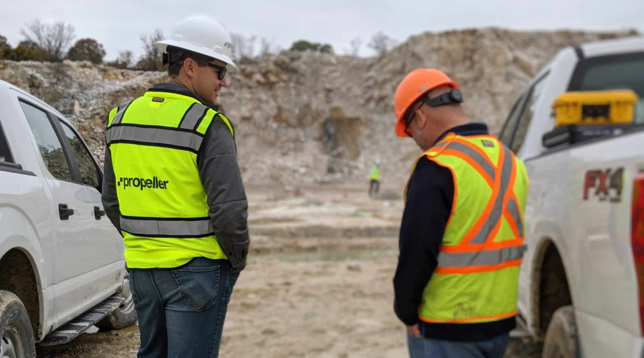 Two construction men on site stood next to two trucks.
