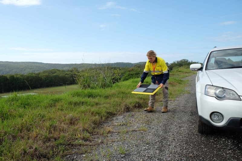 A surveyor laying an AeroPoint on the ground stood next to a car.