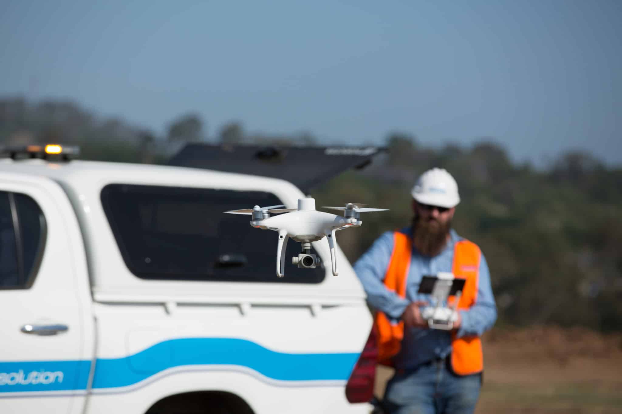 A Drone in flight with the pilot in the background out of focus.