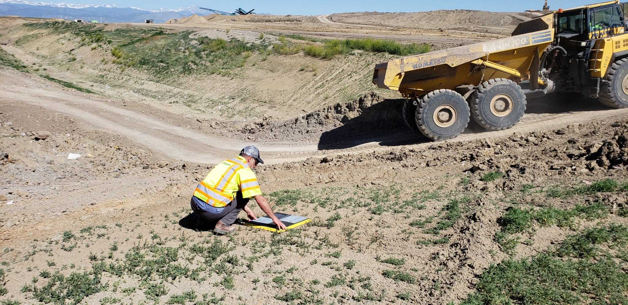 Site worker laying an AeroPoint on the side of a dirt track with a truck driving by.