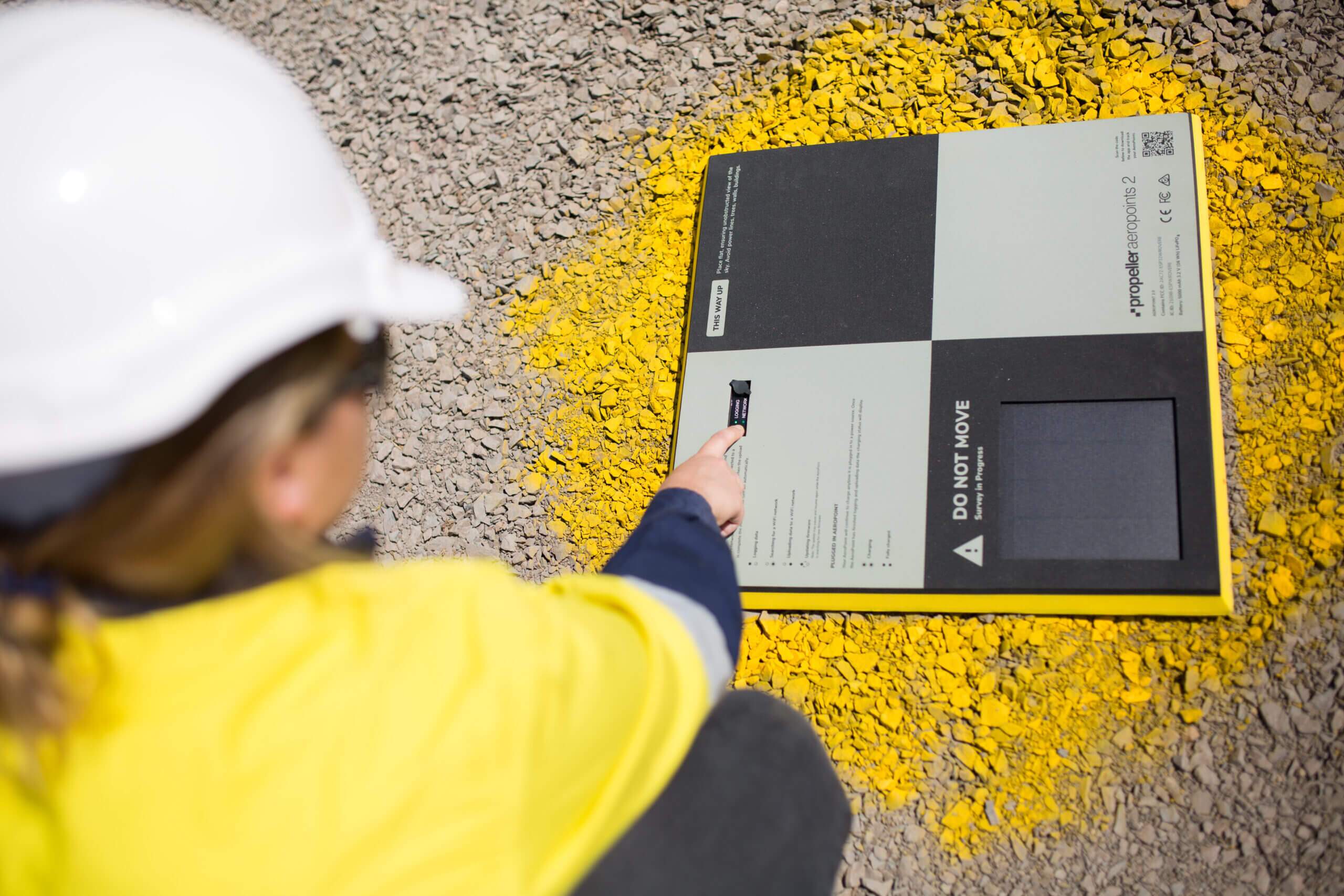 Person turning on an AeroPoint unit on a construction site wearing a hi-vis vest and hardhat