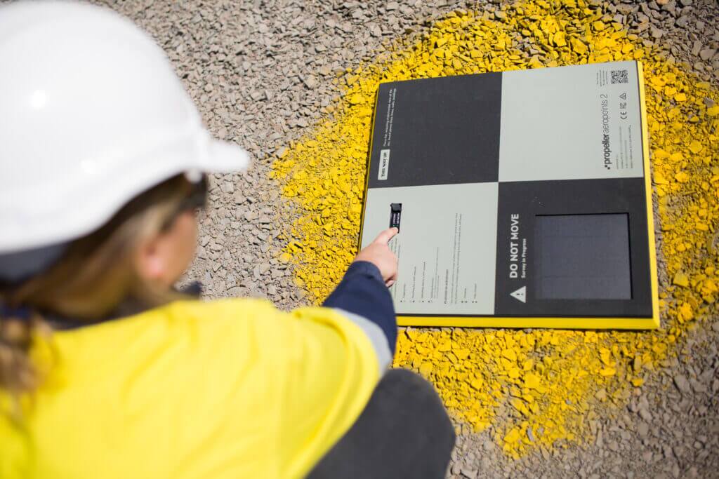Person turning on an AeroPoint unit on a construction site wearing a hi-vis vest and hardhat