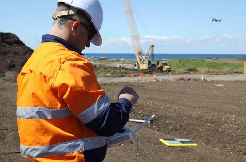 Drone pilot in hi-vis flying a drone next to a crane, with an AeroPoint on the floor.