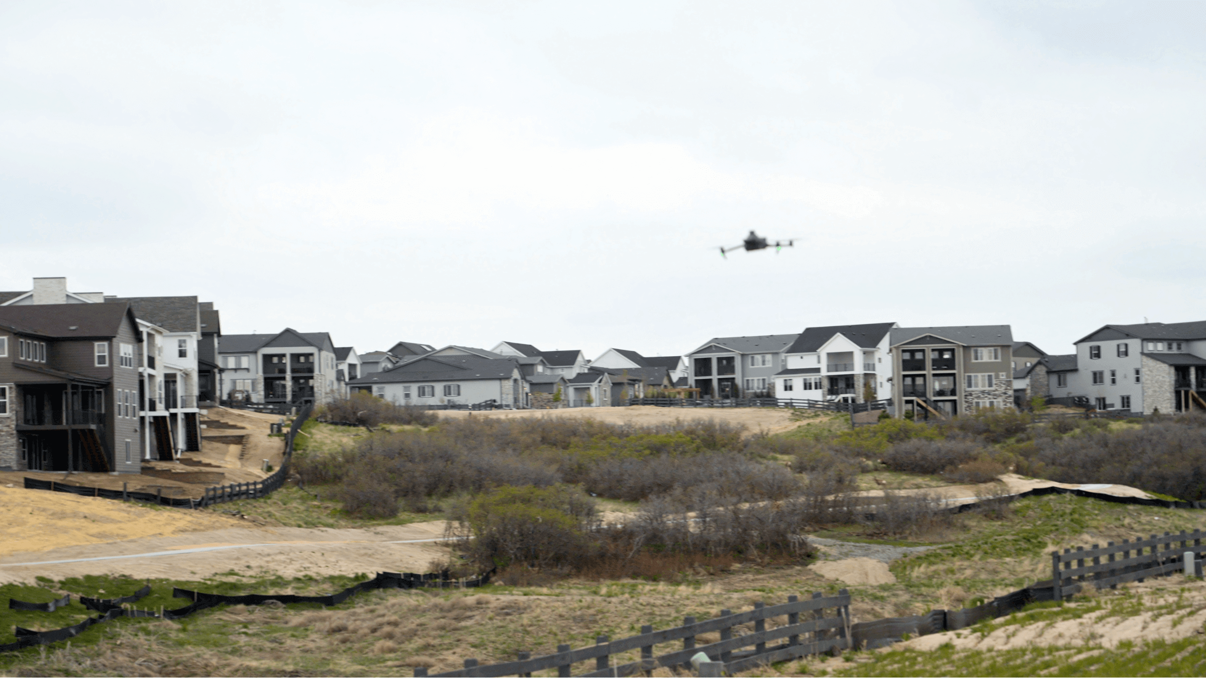 A drone flying over scrub land next to a housing estate.