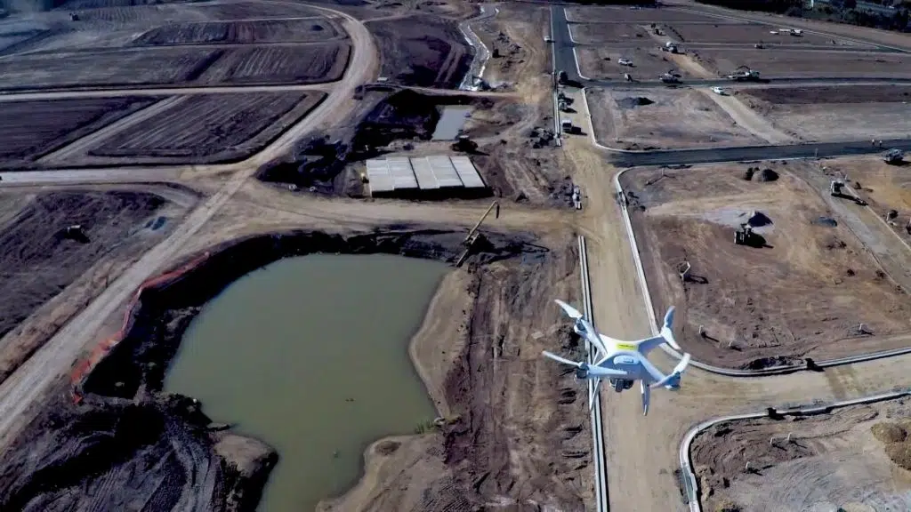 An aerial photo from one drone looking down at a second drone flying above earth earth-moving site.